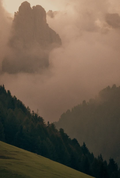 Mglisty widok na leśne zbocza i skaliste szczyty w tle.